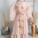 Studio portrait of a woman wearing a pink abaya with golden embroidery and a headscarf.
