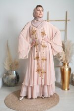 Studio portrait of a woman wearing a pink abaya with golden embroidery and a headscarf.