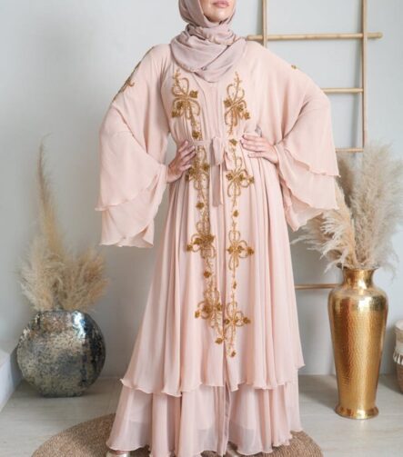 Studio portrait of a woman wearing a pink abaya with golden embroidery and a headscarf.