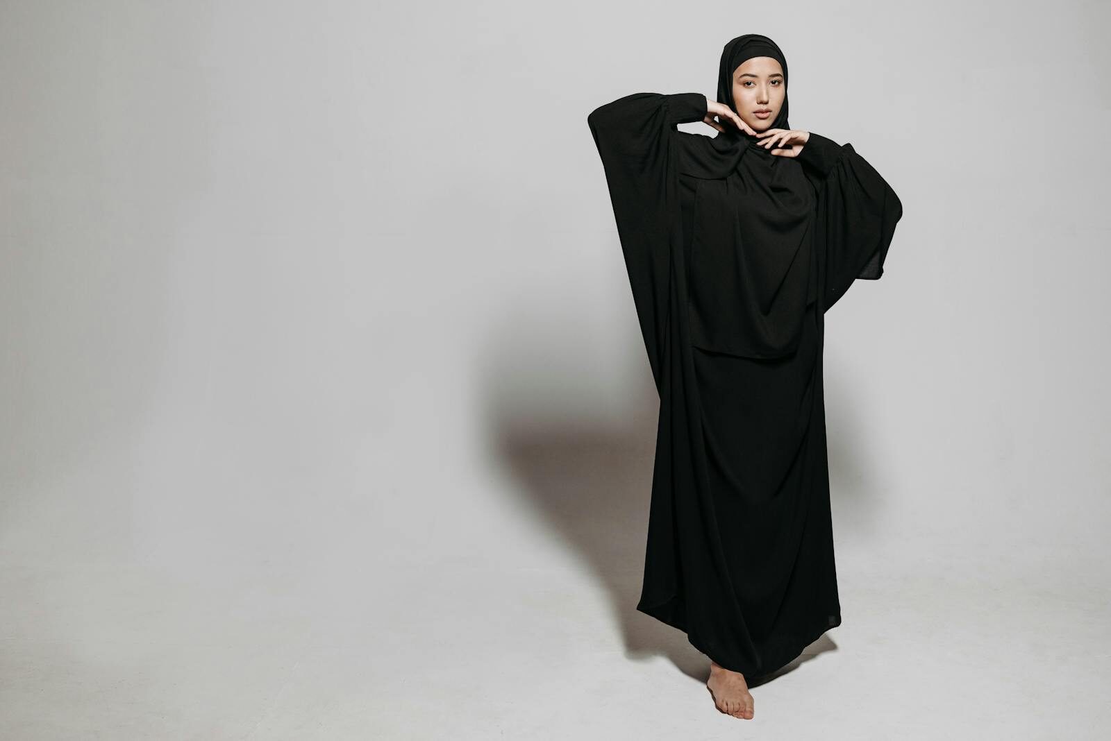 Portrait of a woman in a stylish black abaya striking a pose on a neutral background.